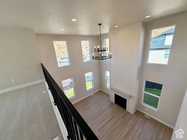 Open-concept living space featuring high ceilings, wood-finish flooring, a fireplace with a light-toned mantel, multiple windows, and a black wrought-iron chandelier