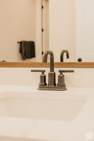Undermount sink with stone-finish countertop, dark metal widespread faucet, and wood-framed mirror