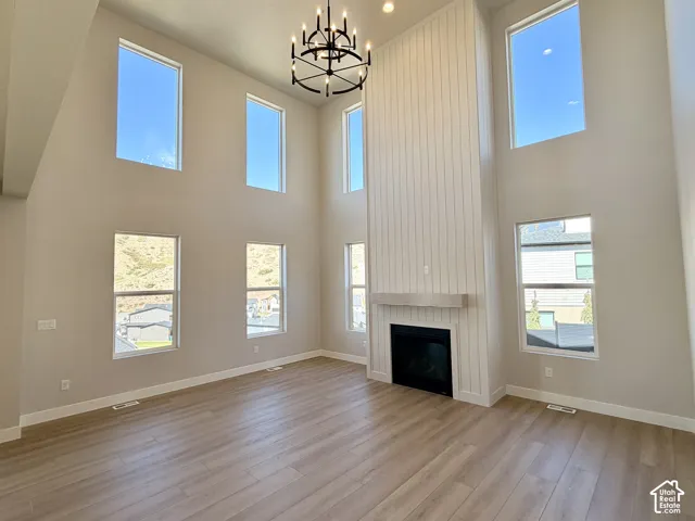 Vaulted ceilings with a prominent black chandelier, wood-finish flooring, and a fireplace with a light wood mantle