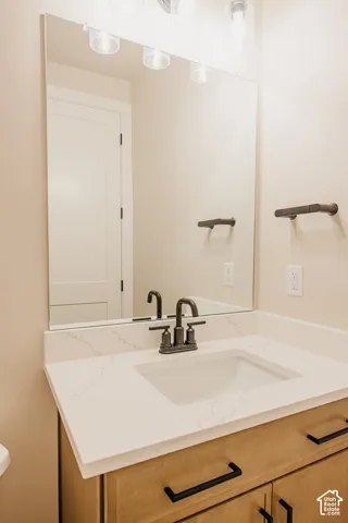 Vanity with stone countertop, undermount sink, matte black widespread faucet, wood-finish cabinetry with bar pulls, and a frameless mirror