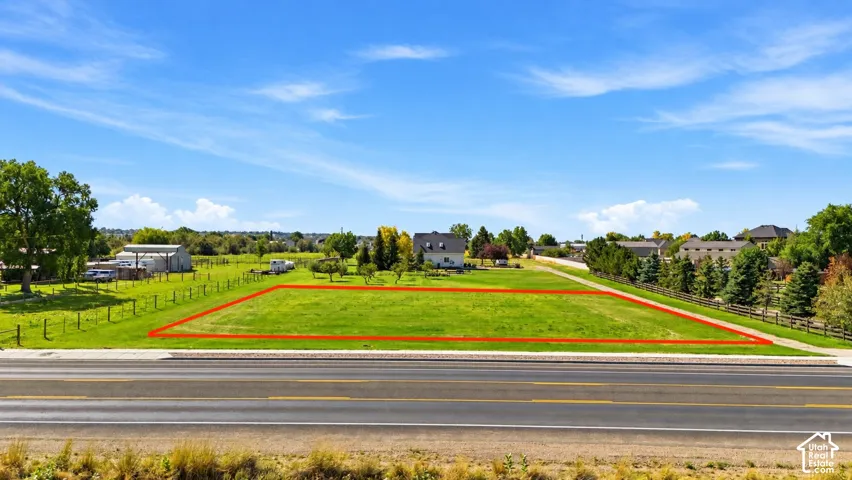 Expansive grassy lot with mature perimeter trees, bordered by a paved roadway