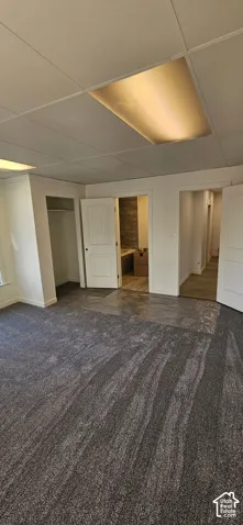 Recessed lighting, drop ceiling, dark patterned carpeting, white interior doors, and a tiled wall feature