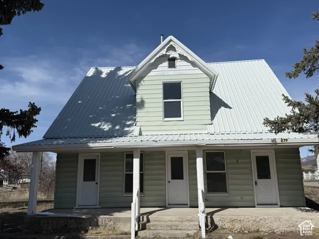Light green horizontal siding exterior with a white metal roof, featuring a covered porch with white columns, and multiple windows and doors