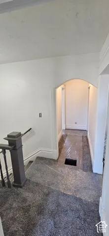 Archway leading to a hallway, with a staircase featuring a dark-toned newel post and balusters