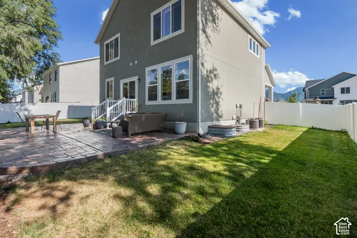 Rear exterior with a stamped concrete patio, white vinyl fencing, and a manicured lawn