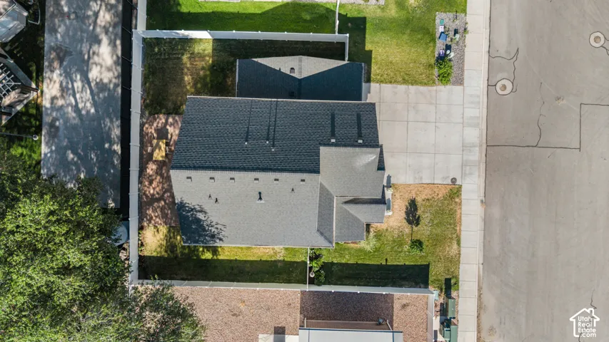 Pitched roof structure, asphalt shingles, concrete driveway, fenced perimeter, and landscaped grounds
