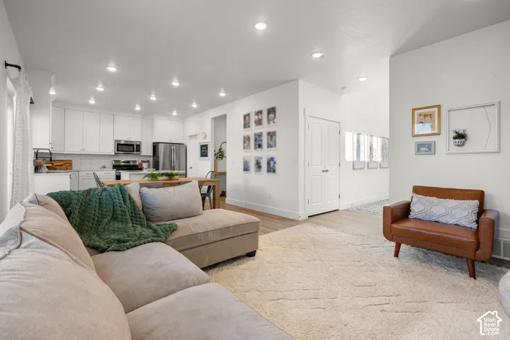 Open-concept living space featuring recessed lighting, light wood-finish flooring, white kitchen cabinetry, stainless steel appliances, and a tiled kitchen backsplash
