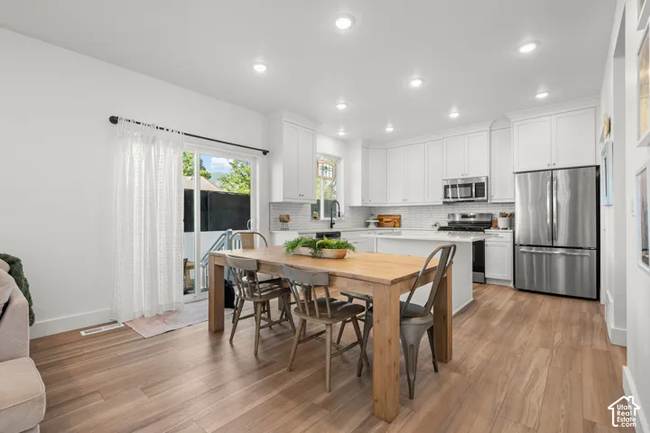 Wood-finish flooring throughout, bright white walls, recessed lighting, and a modern kitchen featuring stainless steel appliances and white cabinetry