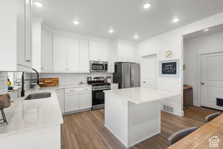 White cabinetry, stainless steel appliances, light-toned countertops, wood-finish flooring, and recessed lighting