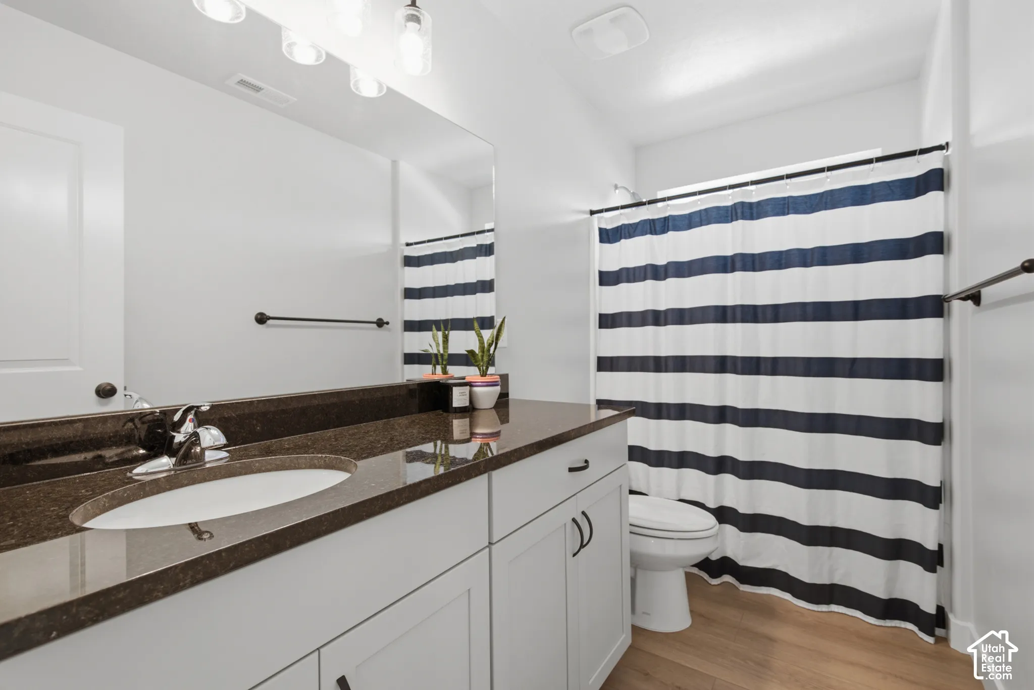 White vanity with integrated sink, dark countertop, chrome faucet, and wood-finish flooring