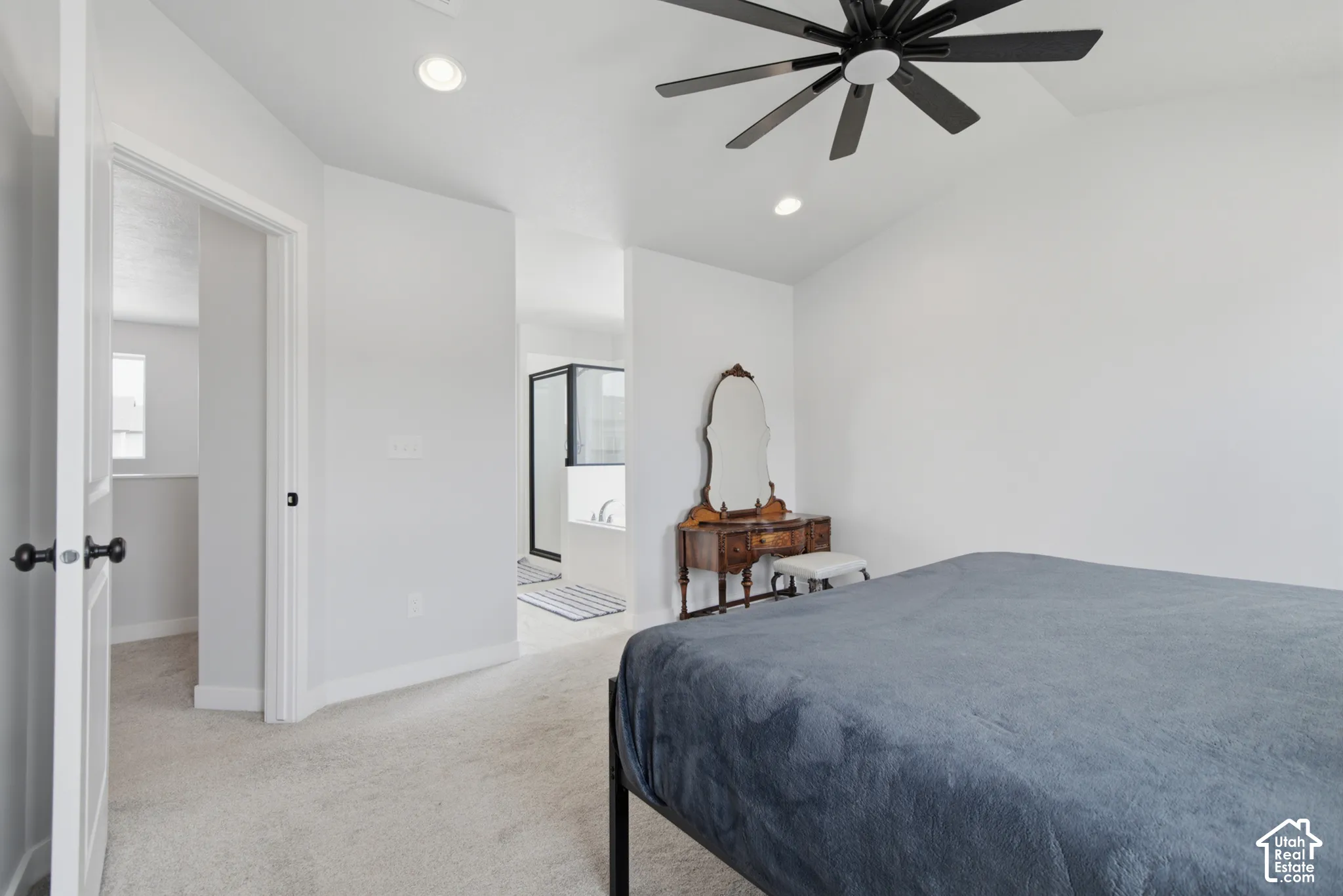 Vaulted ceiling with an attached ceiling fan, recessed lighting, light-colored carpeting, and a doorway leading to an adjoining bathroom with a built-in tub and a shower enclosure