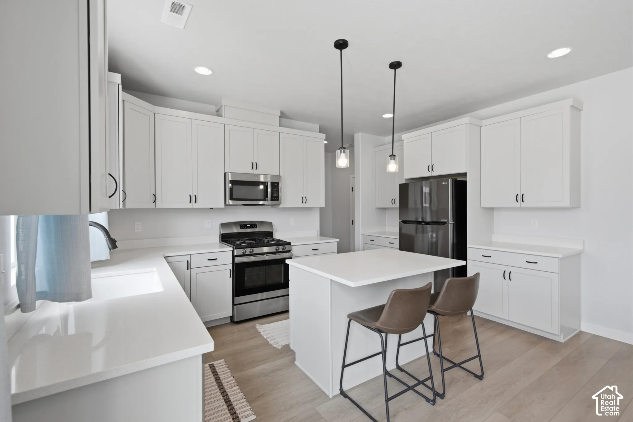 White shaker cabinetry with black hardware, stainless steel gas range, built-in microwave, white countertops, and recessed lighting