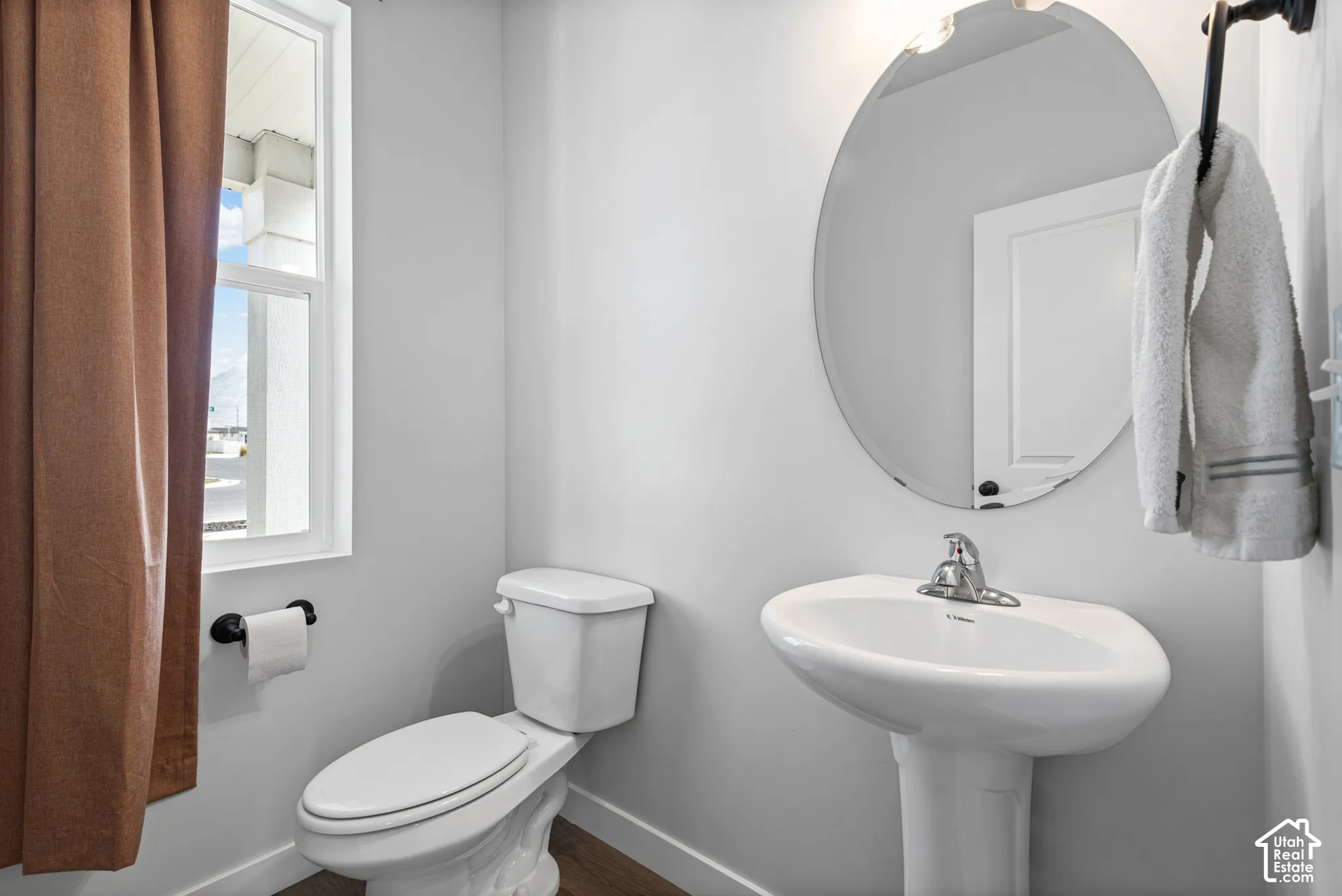Pedestal sink with chrome-finish faucet, oval mirror, and wood-finish flooring