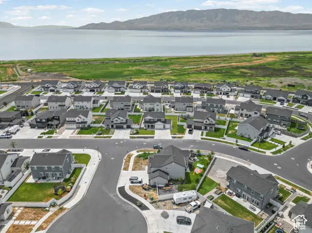 Residential neighborhood featuring paved streets and sidewalks, individual homes with landscaped yards, and a backdrop of a large lake and distant mountains