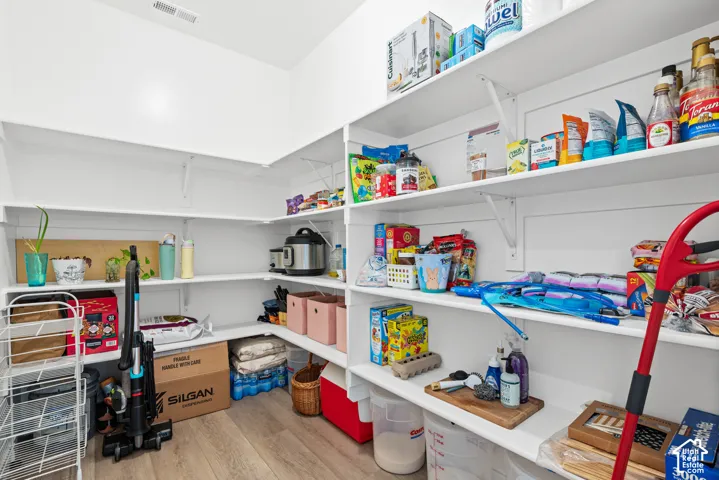 Pantry featuring multiple white shelves, wood-finish flooring, and white walls