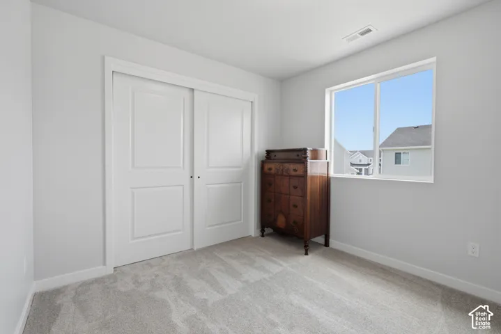 Light grey walls with a large window, light grey carpet, and white sliding closet doors
