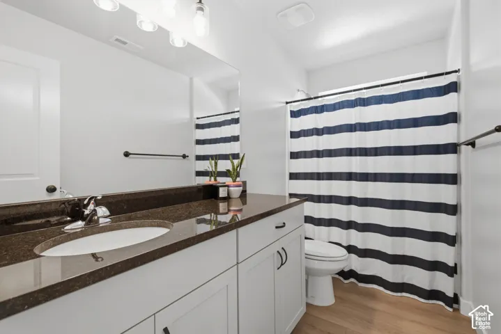 White vanity with integrated sink, dark countertop, chrome faucet, and wood-finish flooring