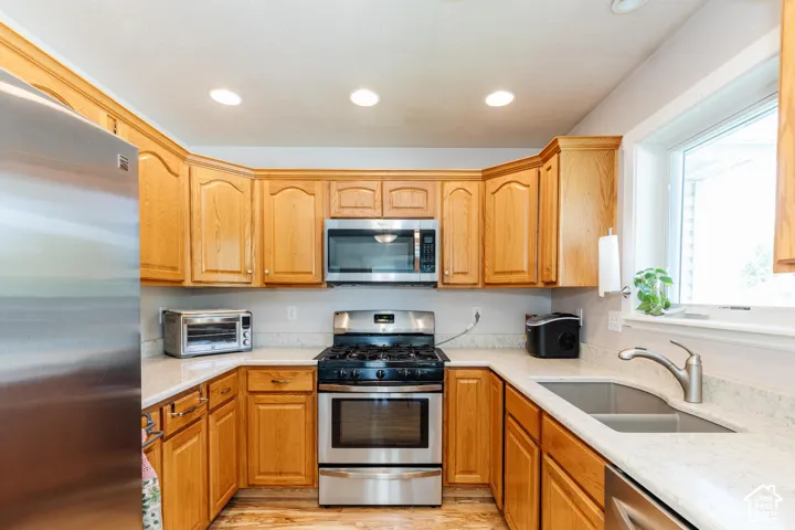 U-shaped kitchen with wood-finish cabinetry, light-toned countertops, stainless steel appliances, and a double basin sink