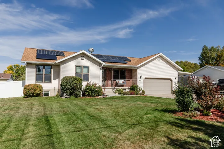 Exterior featuring solar panels, attached garage, front porch, and a manicured lawn