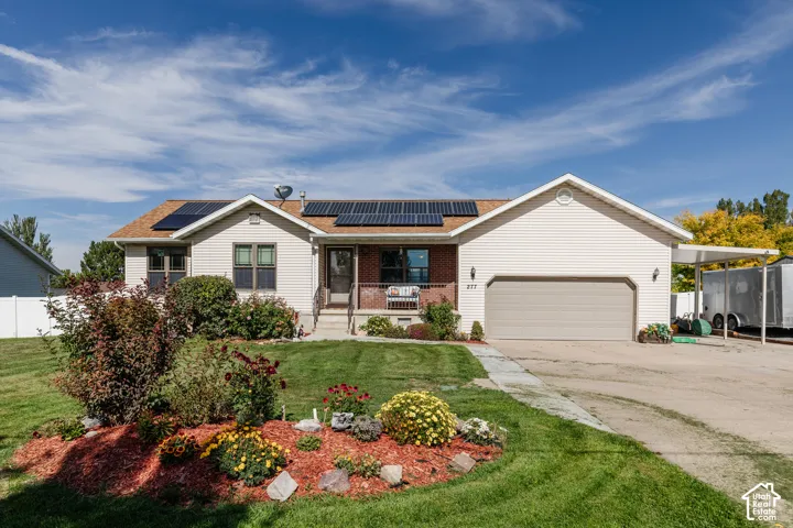 Single-story residence featuring a two-car garage, solar panels, a covered front porch, a carport, and a landscaped front yard with mature plantings