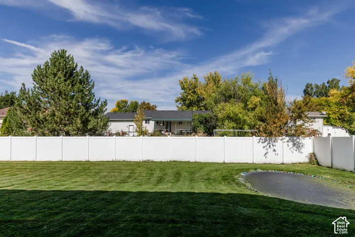 Expansive backyard featuring a manicured lawn, white privacy fencing, and mature trees