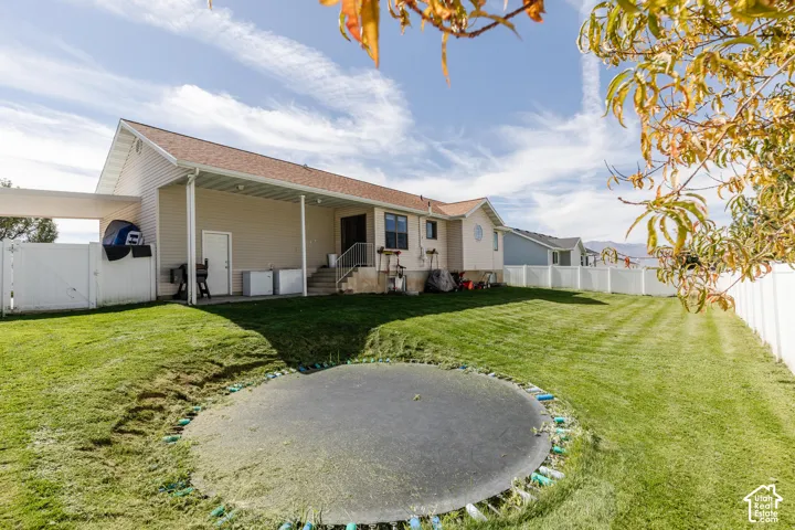 Expansive rear yard featuring green lawn, a white privacy fence, and a covered patio