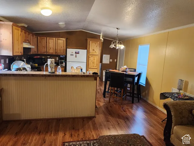 Wood-finish flooring throughout, wood cabinetry, built-in breakfast bar with beadboard paneling, chandelier lighting, and a white refrigerator