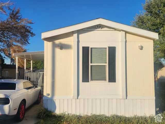 Cream-colored siding exterior with white trim, dark window shutters, and a covered carport