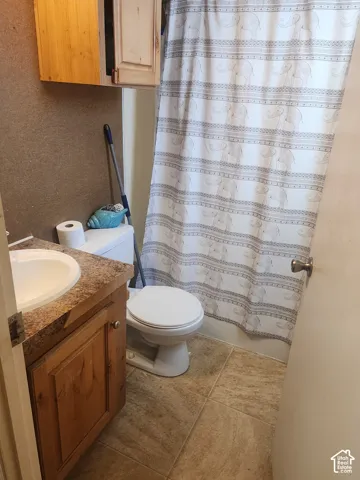 Floor-mounted toilet, vanity with integrated sink, patterned shower curtain, wall-mounted cabinetry, and tile flooring
