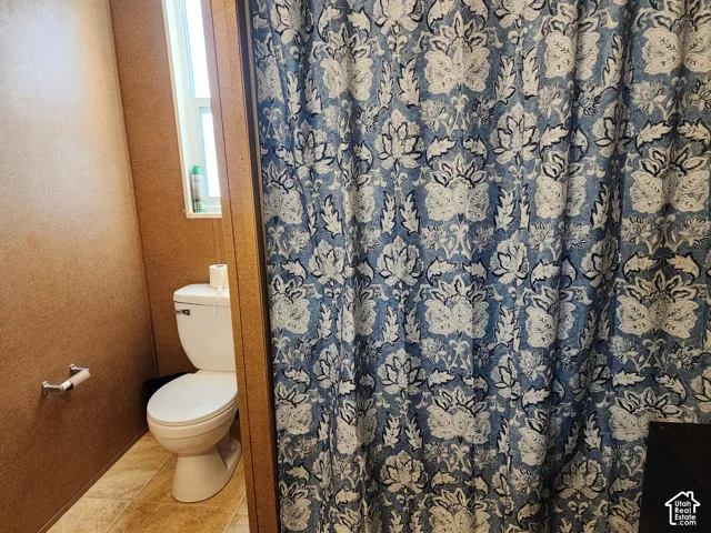 White toilet with a dual-flush mechanism, chrome toilet paper holder, and a frosted window