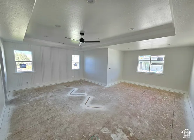 Tray ceiling with recessed lighting, ceiling fan, decorative wall paneling, and multiple windows