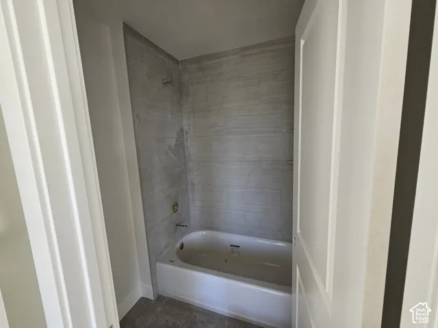 Bathtub with brass fixtures, textured tile shower surround, and tile flooring