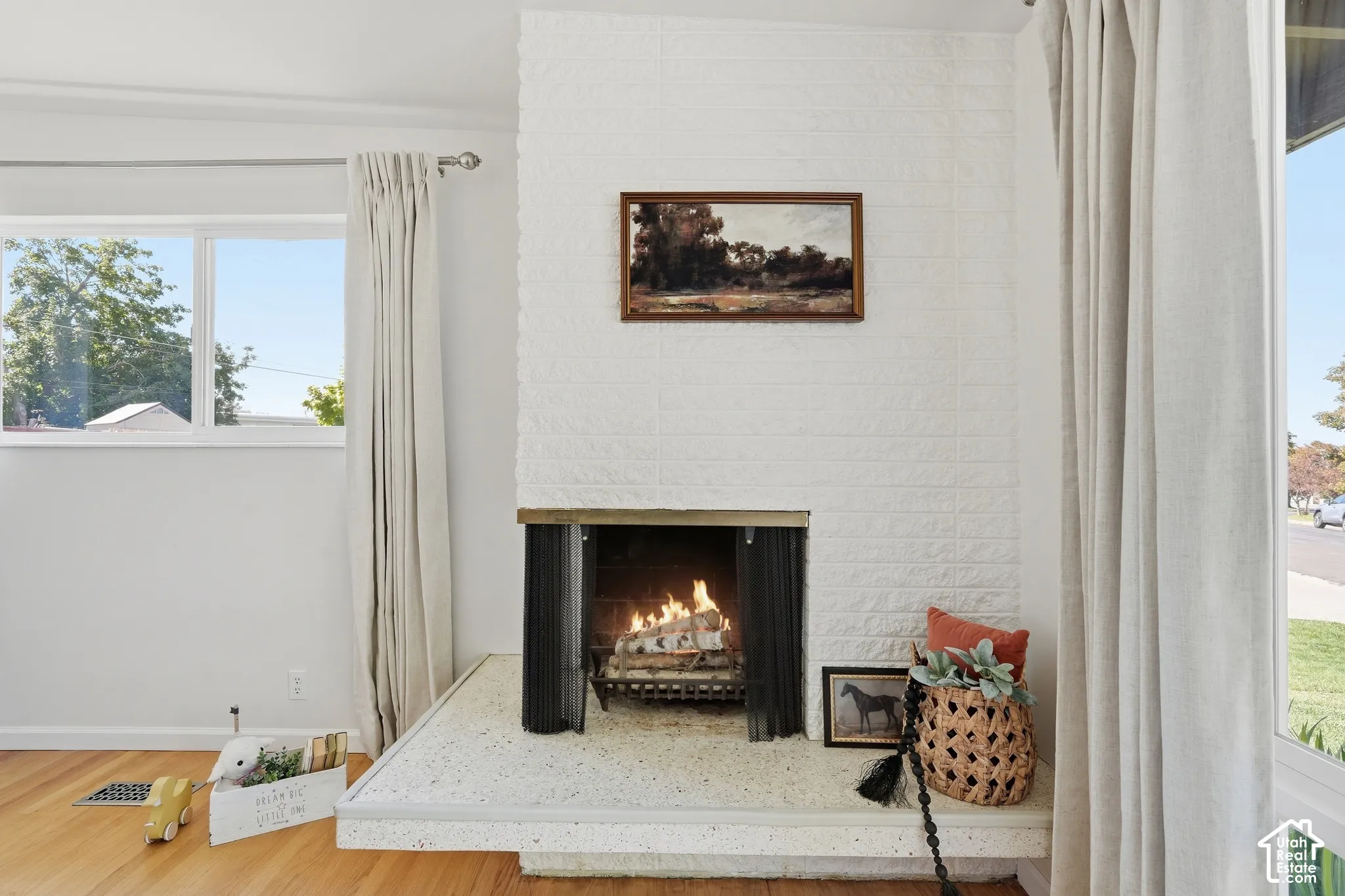 White brick fireplace with an elevated hearth, wood-finish flooring, and white walls