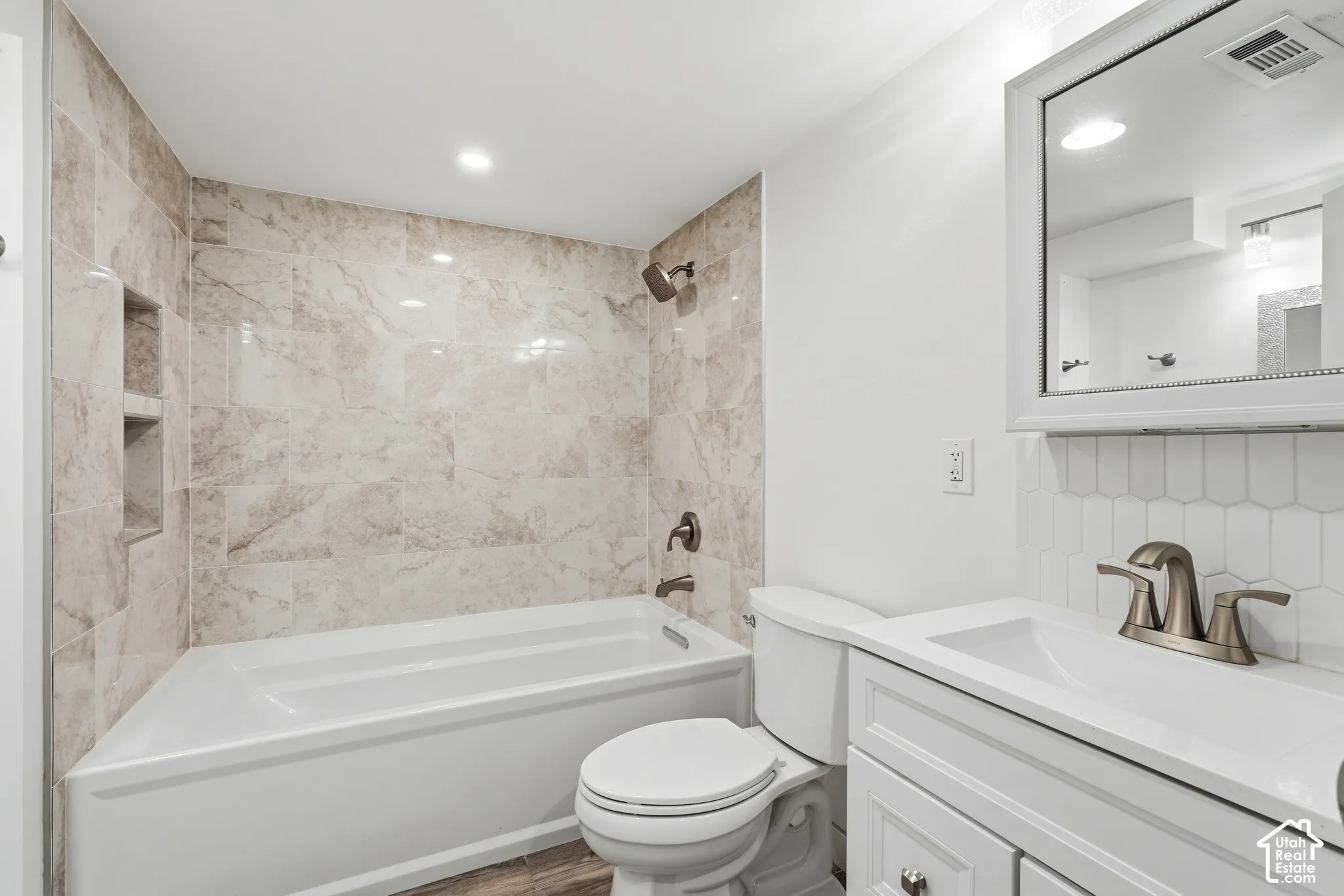 Bathroom featuring a soaking tub, tile shower surround with recessed shelving, wood-finish flooring, a white vanity with an integrated sink, and a framed mirror
