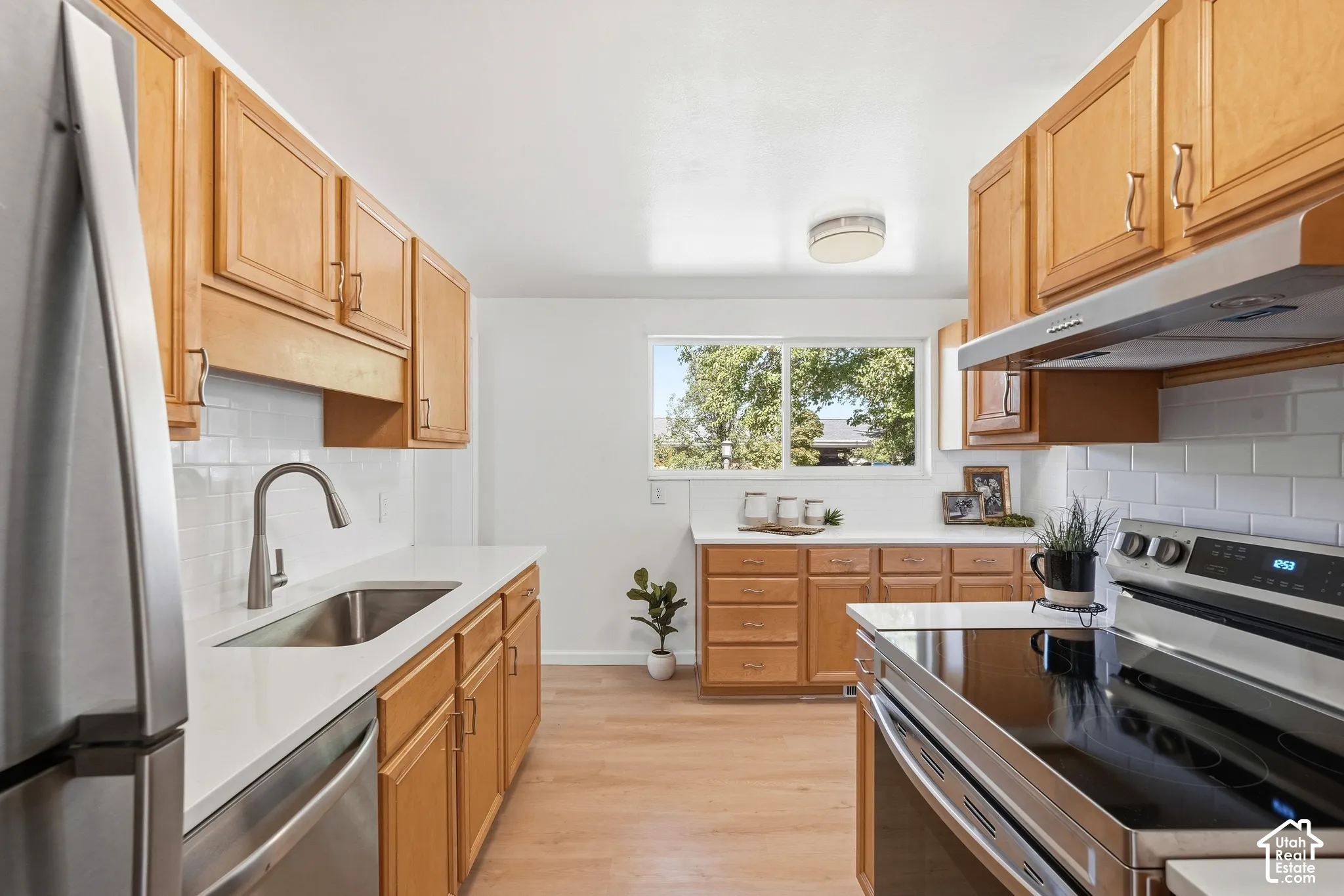 Kitchen featuring wood cabinetry, white countertops, stainless steel appliances, white subway tile backsplash, and wood-finish flooring