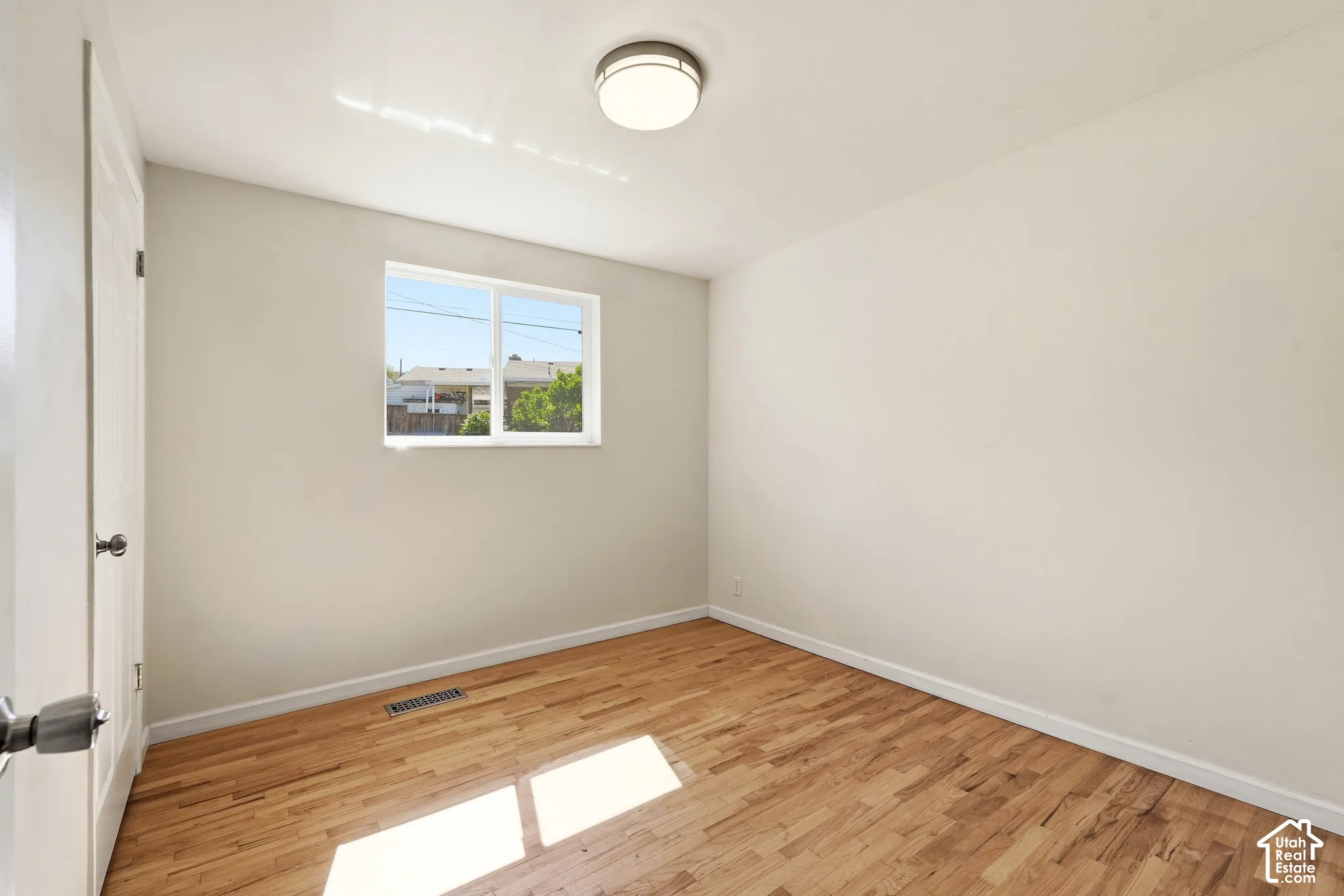Hardwood flooring, painted walls, window with white trim, white door, and flush-mount ceiling light