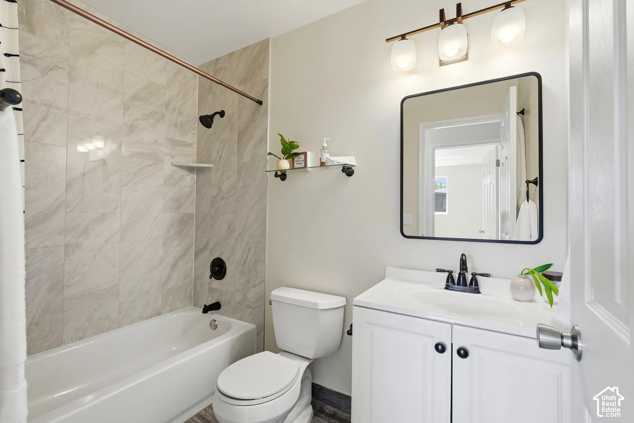 Tub/shower combination with tile surround, white vanity with cabinet storage, matte black faucet, and rectangular framed mirror