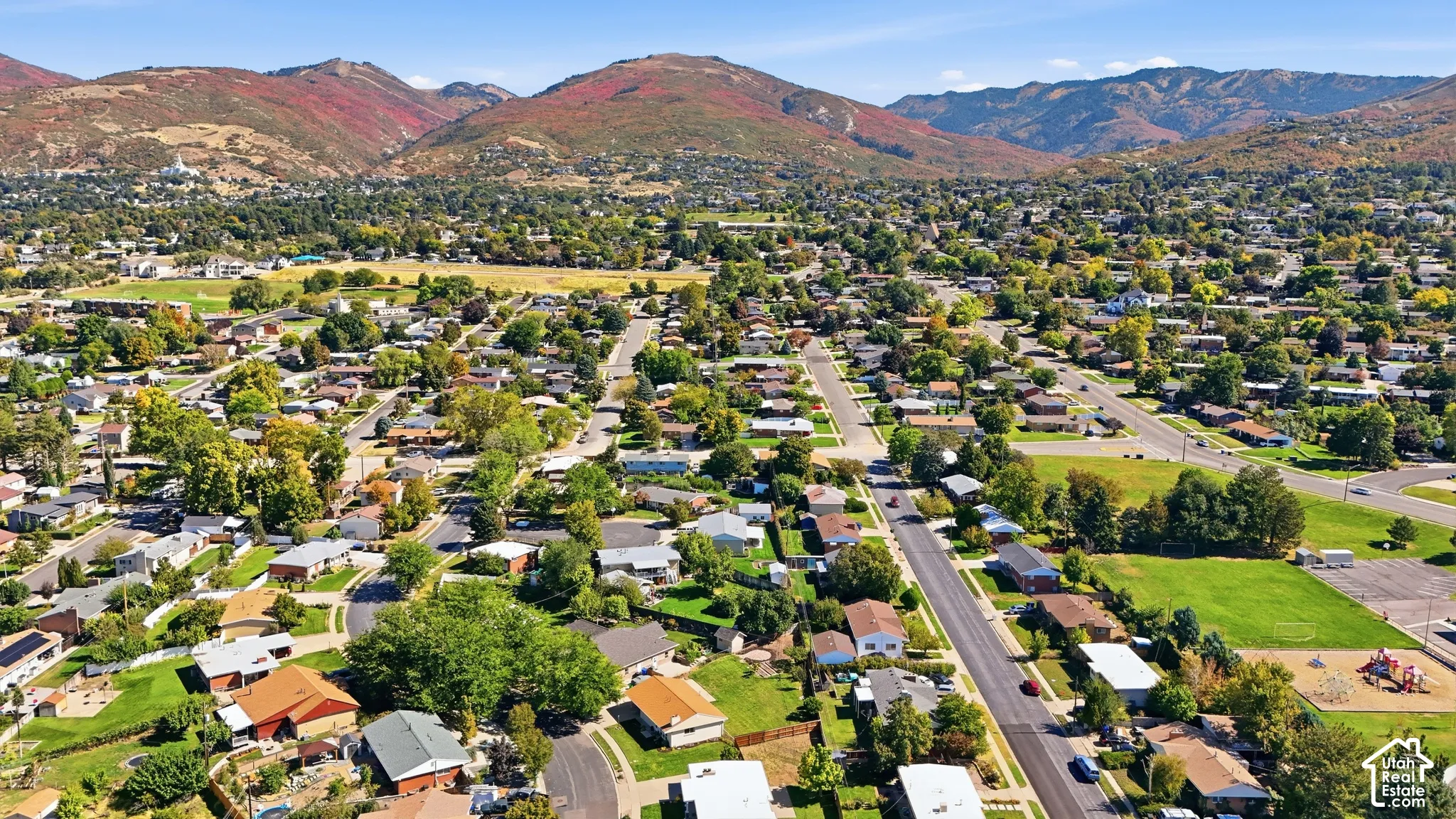 Mountain backdrop with a residential neighborhood featuring established trees, paved roads, and a playground area