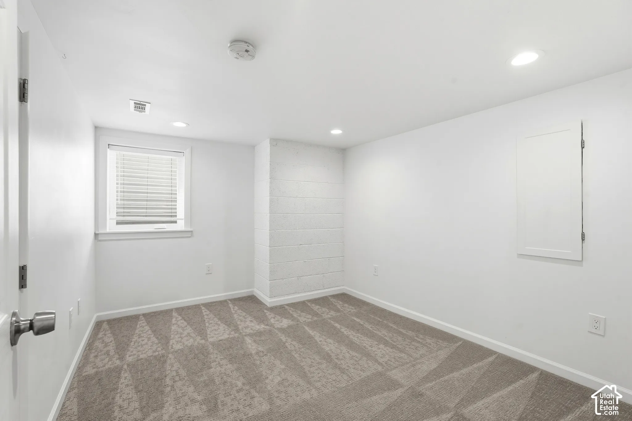 Recessed lighting, patterned carpet, window with blinds, and painted block wall