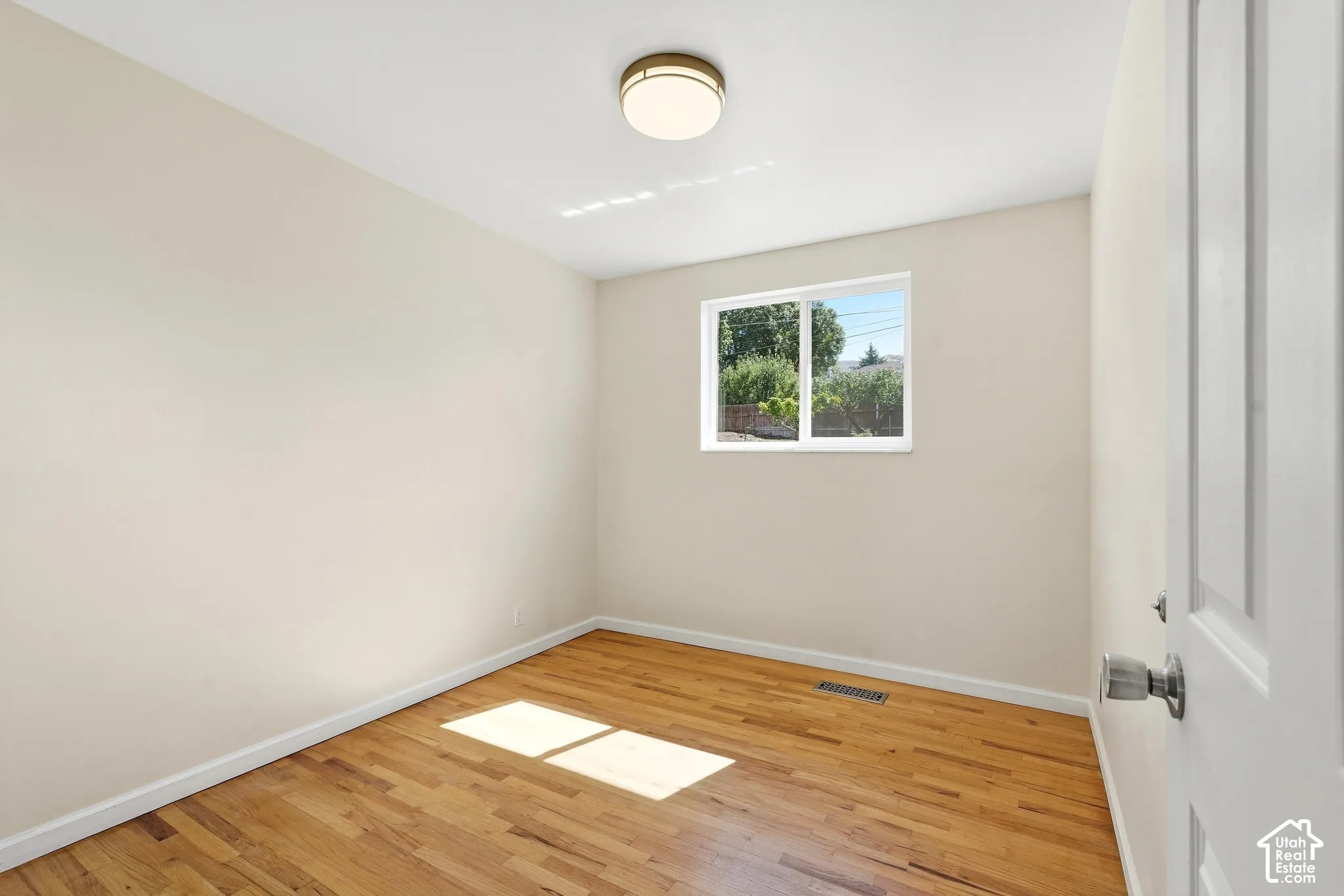 Wood-finish flooring, single window, flush mount ceiling light, white panel door, and neutral wall tones
