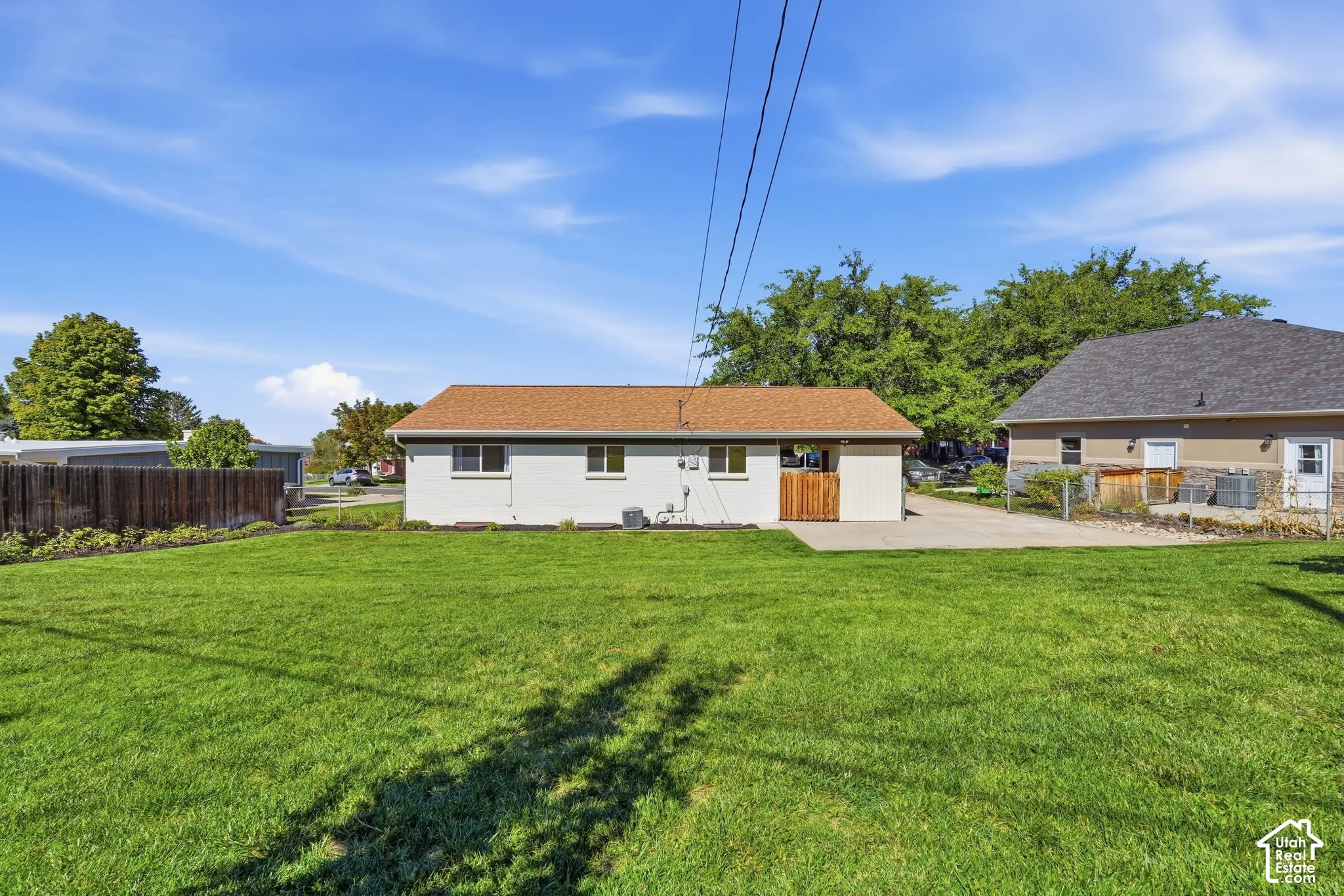 Expansive green lawn, wood fence, concrete driveway, and a tan exterior with a brown roof