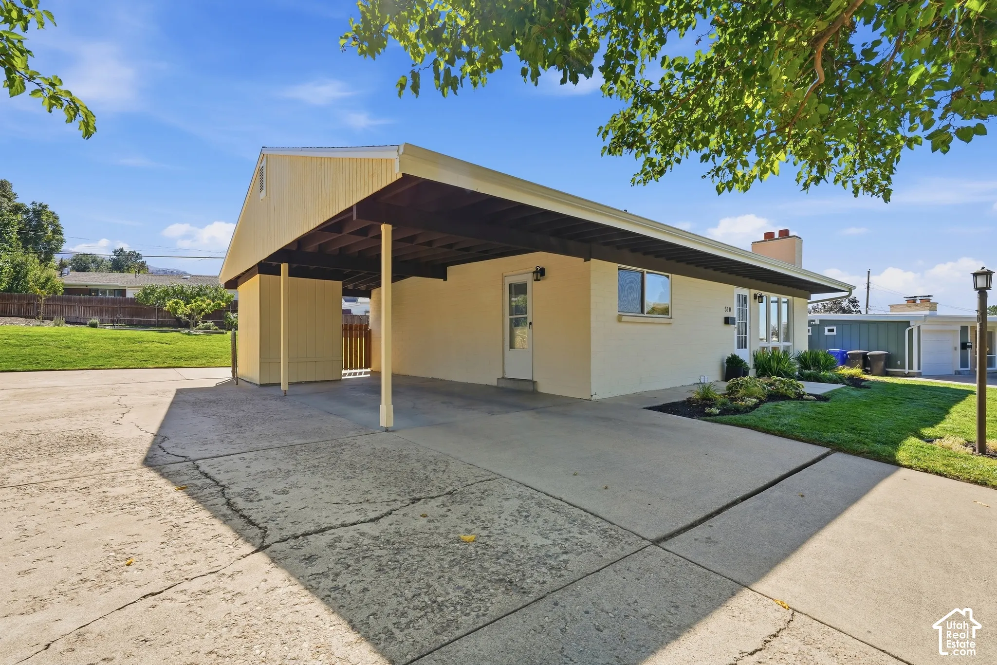 Single-story exterior with a covered carport, manicured front lawn, and landscaped planting beds