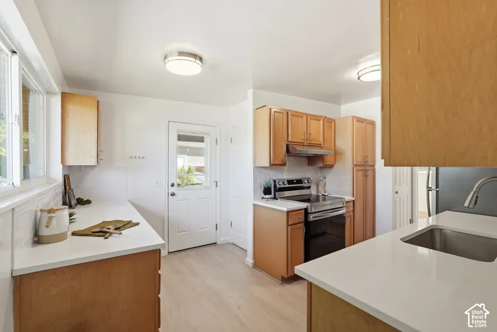 Light wood-finish cabinetry with stainless steel hardware, white countertops, stainless steel appliances, and wood-finish flooring