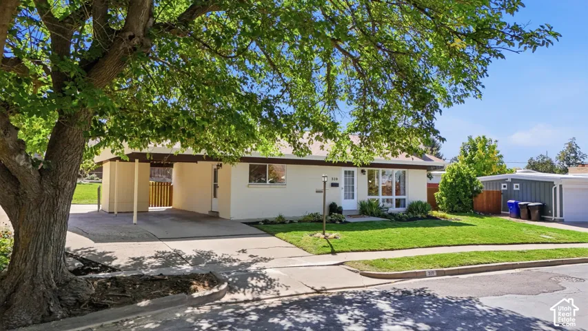 Exterior featuring a carport, front lawn, mature shade tree, and established landscaping