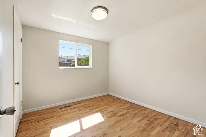 Hardwood flooring, painted walls, window with white trim, white door, and flush-mount ceiling light