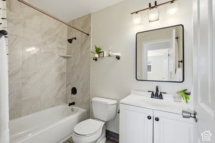 Tub/shower combination with tile surround, white vanity with cabinet storage, matte black faucet, and rectangular framed mirror