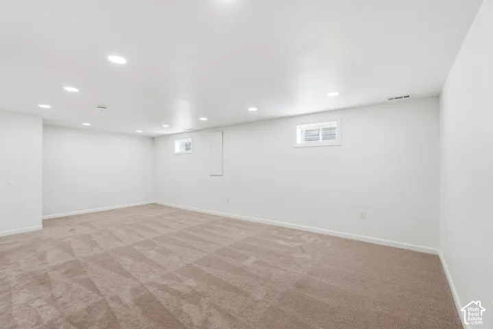 Recessed ceiling lighting, white painted walls, two windows, and patterned carpeting