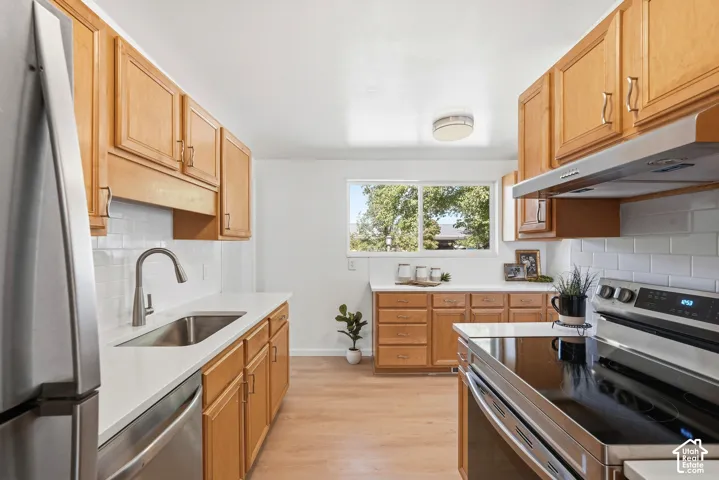Kitchen featuring light wood cabinetry, stainless steel appliances, white subway tile backsplash, white countertops, and wood-finish flooring