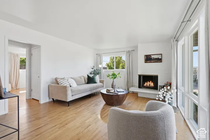 Light wood-finish flooring, white painted walls, white brick fireplace, multiple windows with white trim, and a white interior door