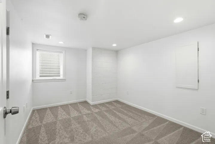 Recessed lighting, patterned carpet, window with blinds, and painted block wall